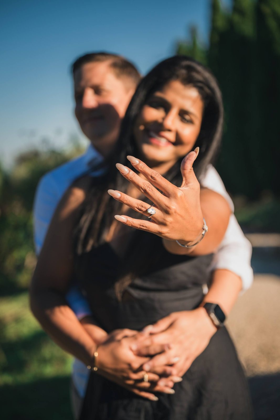 A couple embraces as she holds out her oval engagement ring