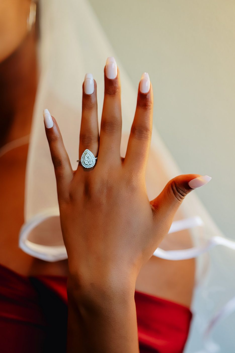A bride in a veil holds up her hand to show a pear-shaped diamond cluster ring
