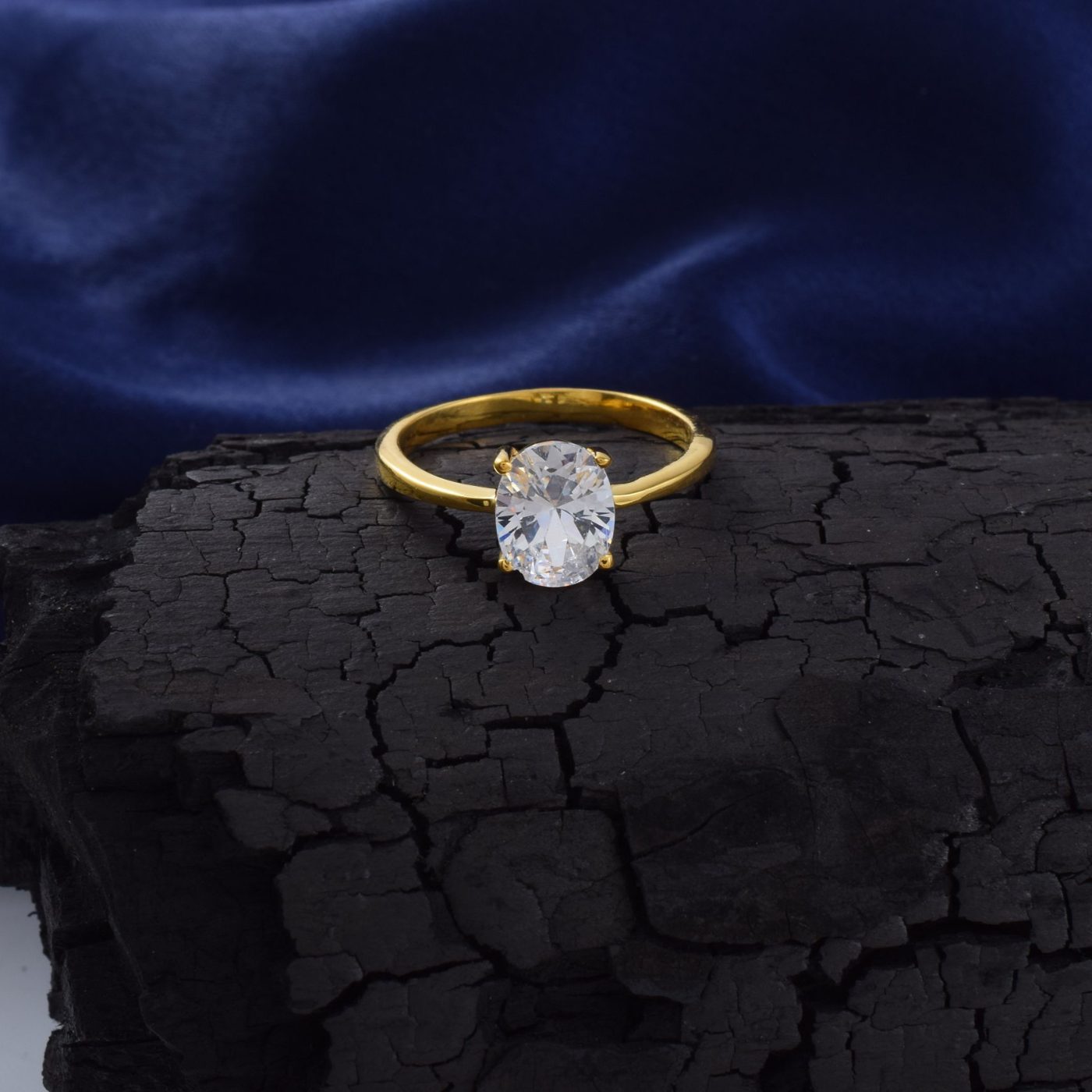 Oval diamond four-prong solitaire in yellow gold on dark stone