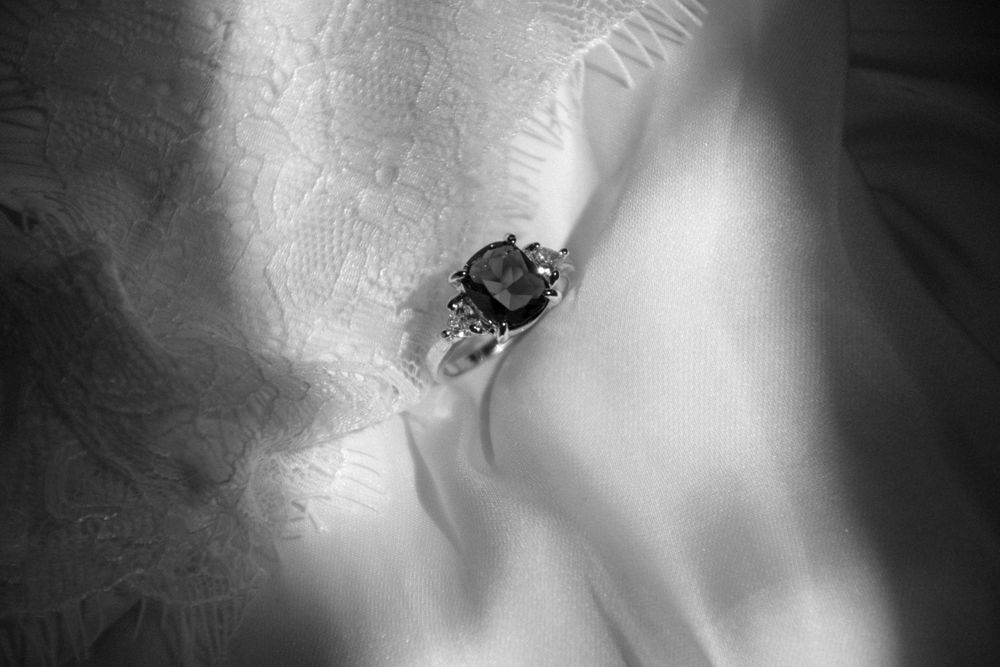 Black-and-white photo of a cushion-cut stone with trillion side stones on lace
