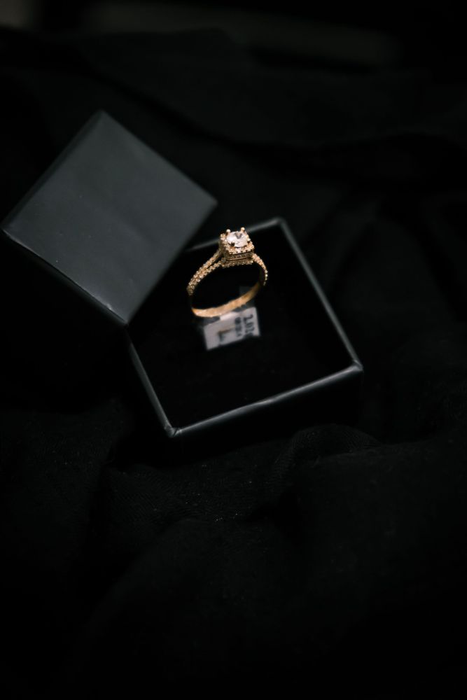 Round diamond in a cushion-shaped halo with a pavé band in yellow gold, in a black ring box