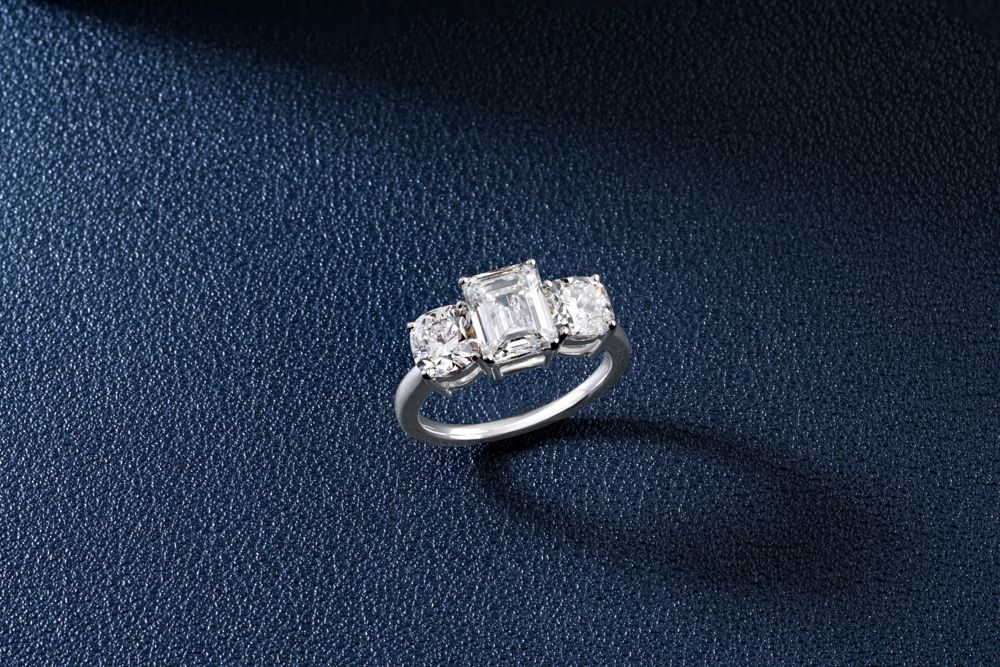 Emerald-cut diamond flanked by two cushion-cut side stones in white gold on navy leather