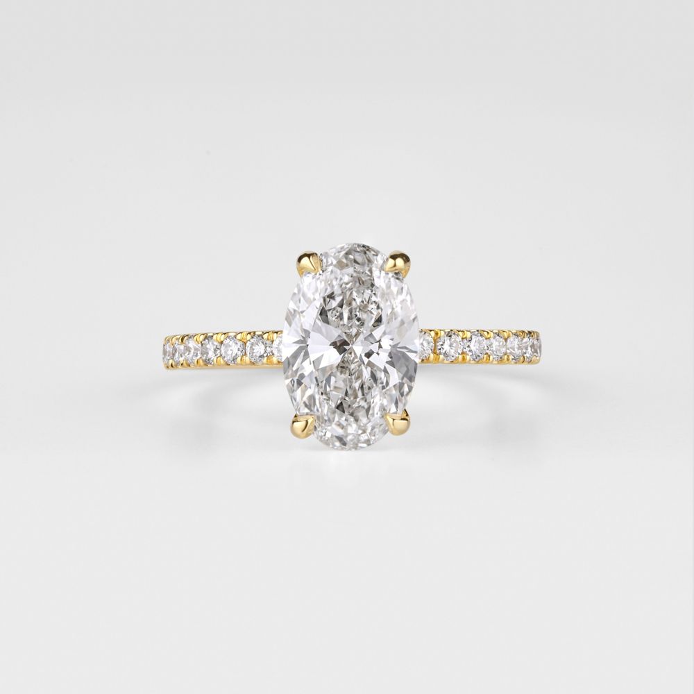 Oval diamond four-prong solitaire with a pavé band in yellow gold on white