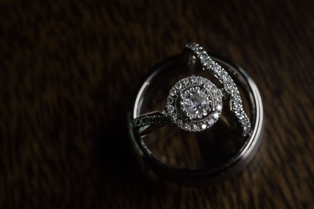 Round halo engagement ring with a curved pavé wedding band, resting inside a men’s band