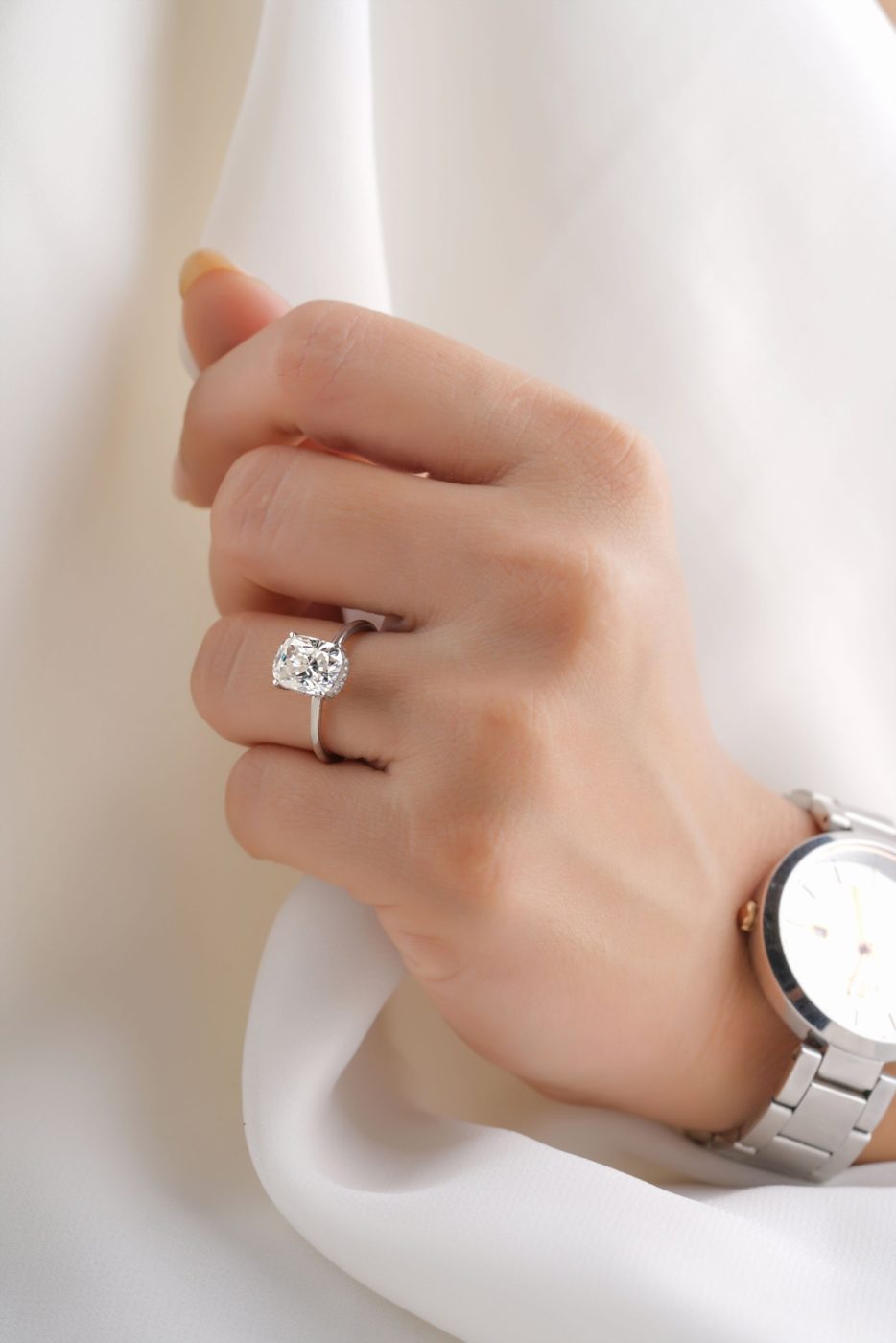 A cushion-cut diamond solitaire worn on a hand against soft white fabric